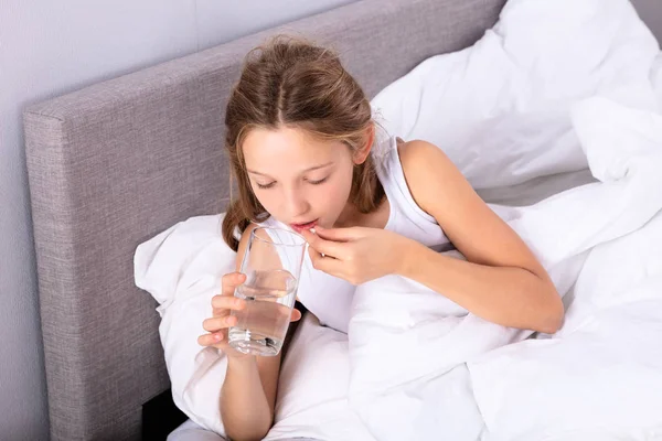 Ragazza Sdraiata Sul Letto Che Prende Medicina Con Bicchiere Acqua — Foto Stock