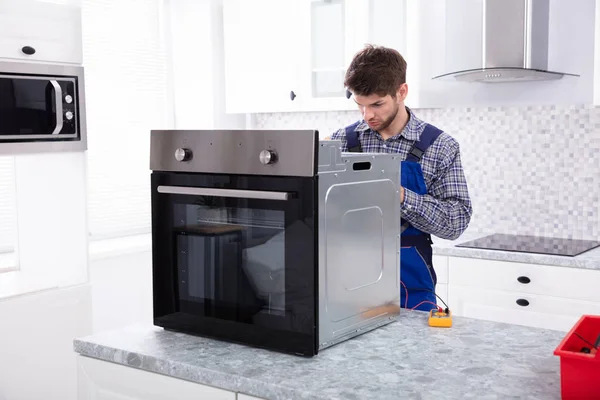 Young Male Repairman Repairing Oven Using Digital Multimeter In Kitchen