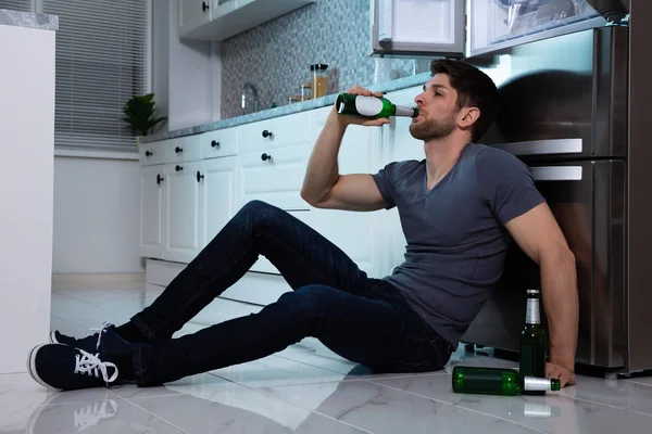 冷蔵庫の前でビールを飲みながら若い男の側面図 — ストック写真