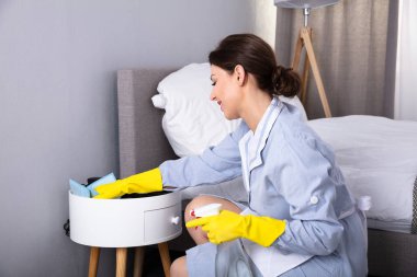 Otel odasında silgi ile mobilya temizleme genç bir hizmetçi yan görünüm