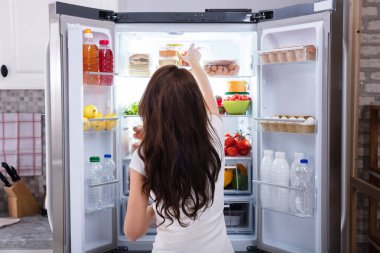 Rear View Of A Young Woman Taking Food To Eat From Refrigerator clipart