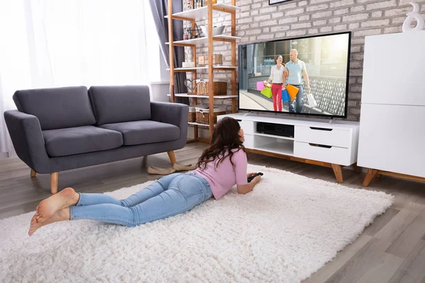 Genç kadın evde televizyon izlerken halı üzerinde yalan rahat