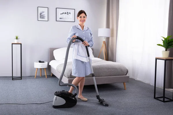 幸せの若い家政婦がホテルの部屋に掃除機でのカーペットの掃除 — ストック写真