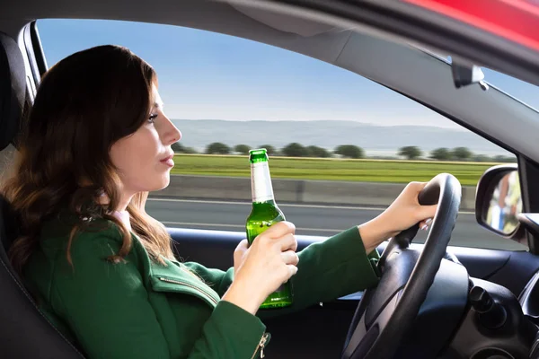 車を運転中にビール瓶を保持している美しい若い女性の側面図 — ストック写真