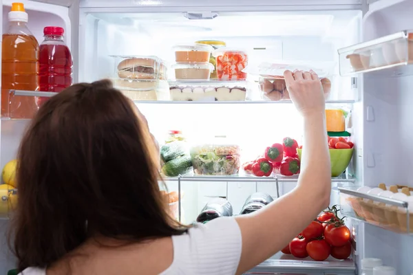 冷蔵庫から食べ物を取っている若い女性の後姿 — ストック写真