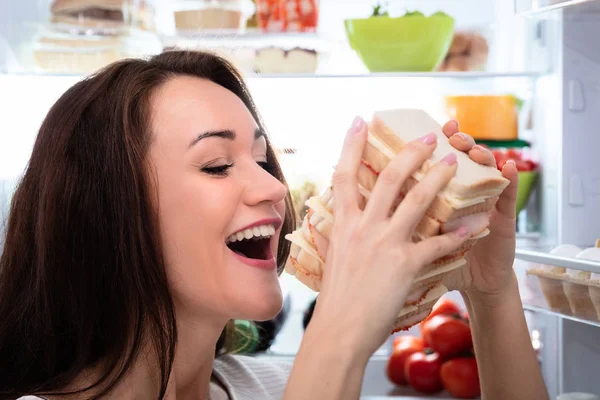 Close Uma Mulher Jovem Com Fome Comendo Sanduíche Perto Geladeira — Fotografia de Stock