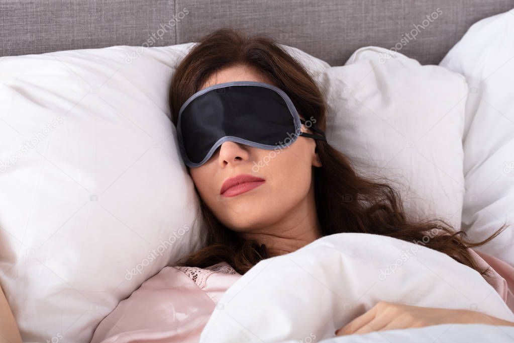 Close-up Of Beautiful Young Woman Sleeping On Bed With Eye Mask