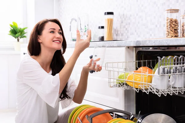Счастливая Молодая Женщина Смотрит Стаканы Возле Посудомоечной Машины — стоковое фото