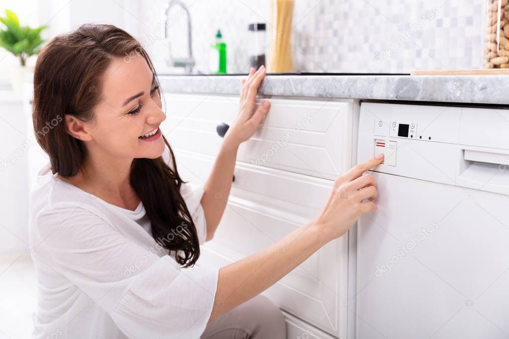 Side View Of A Happy Young Woman Pressing Button Of Dishwasher