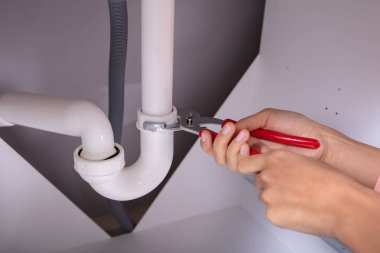 Genç kadın beyaz lavabo boru ayarlanabilir anahtarı ile onarmak A Close-up konsantre