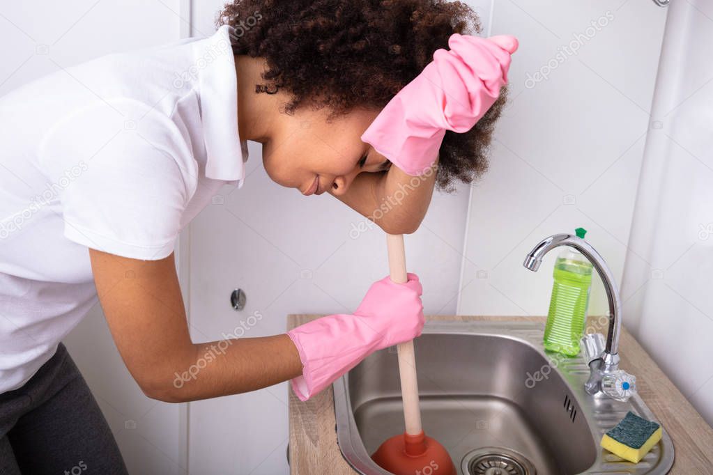Tired Person Wearing Pink Gloves Cleaning Sink Filled With Water With Cup Plunger