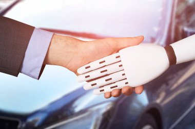 Close-up Of A Man Shaking Hands With Robot In Front Of Car clipart