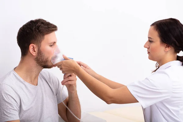 年轻女医生拿着氧气面罩在男性患者的嘴的侧视图 — 图库照片
