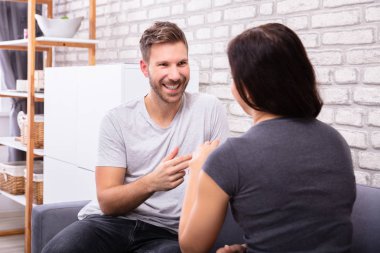 Koltukta oturmuş işaret diliyle iletişim kuran gülümseyen genç çift.