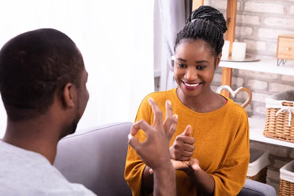 Sorrindo Jovem Casal Sentado Sofá Comunicando Com Línguas Gestuais — Fotografia de Stock