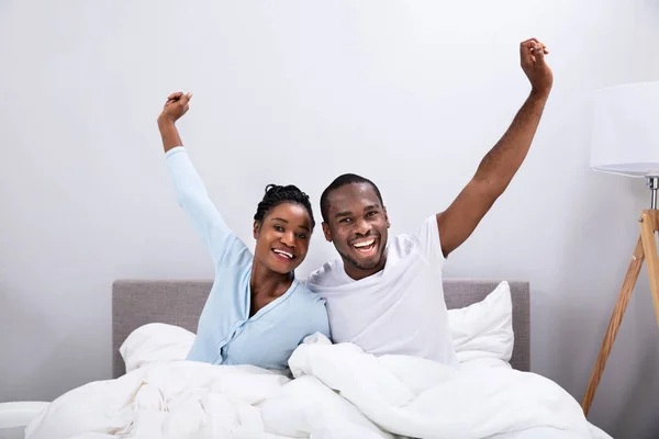 一对快乐的非洲年轻夫妇躺在床上举手表决的画像 — 图库照片