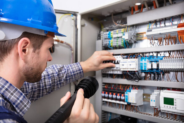 Close-up Of A Electrician Examining A Fuse Box With A Torch
