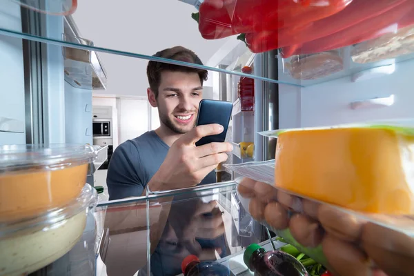 Homem Feliz Frente Geladeira Usando Mobilephone Cozinha — Fotografia de Stock