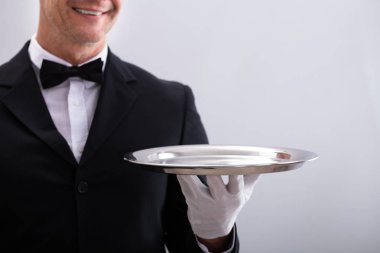 Close-up Of Waiter's Hand Holding Empty Silver Tray Against White Background clipart