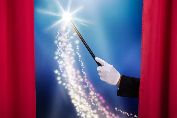 魔術師の手の近くに赤いステージカーテンの後ろに魔法の杖を保持 — ストック写真