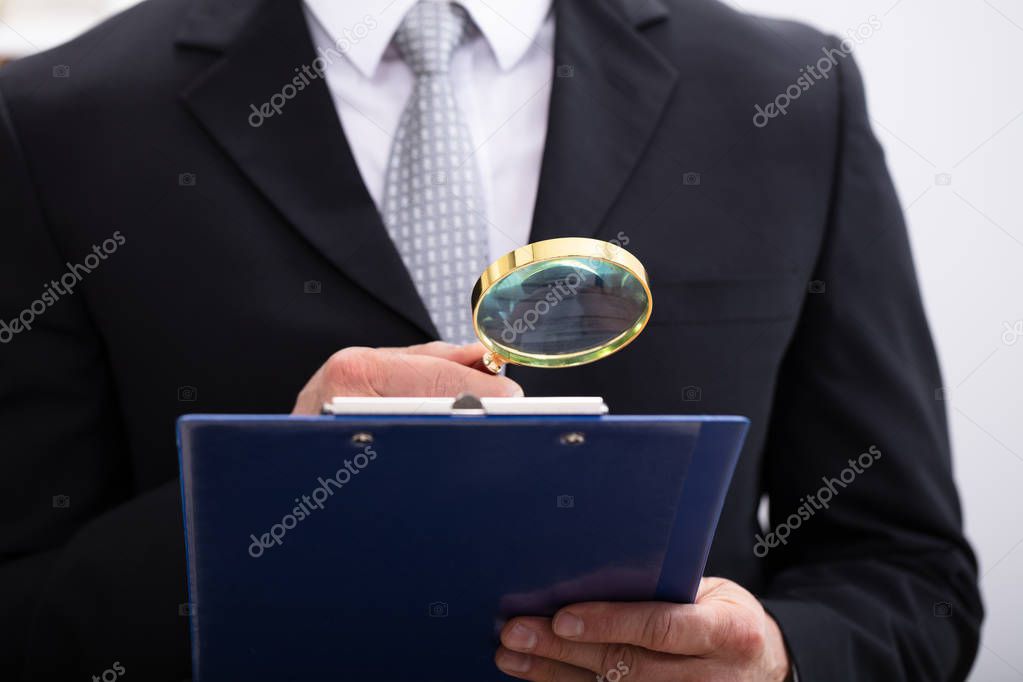 Close-up Of  Businessman Analyzing Document  Through Magnifying Glass At Workplace