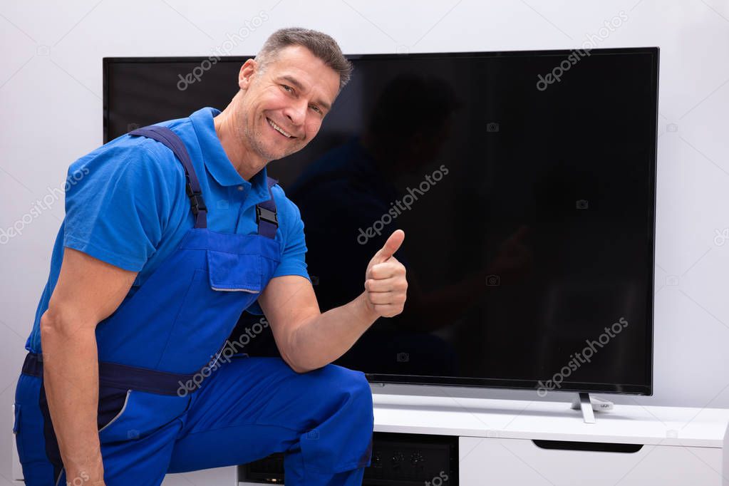 Smiling  Mature Technician Showing Thumb Up In Front Of Television