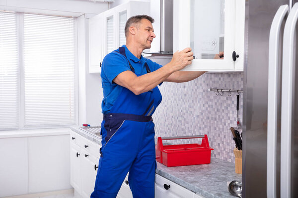 Side View Of Male Handyman Fixing Cabinet Door Using Screwdriver In Kitchen