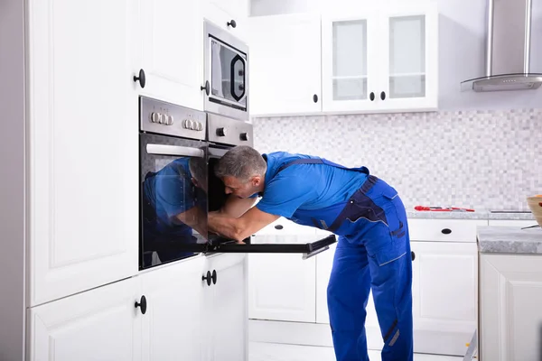 台所でオーブンを全体的に修復する成熟した技術者 — ストック写真