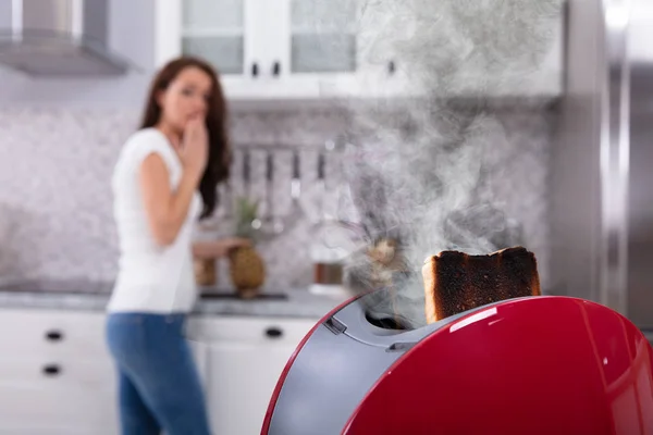 Close-up Of A Red Toaster With Burnt Toast While Woman Working In Kitchen