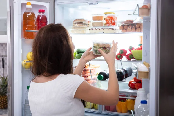 冷蔵庫から食べ物を取っている若い女性の後姿 — ストック写真