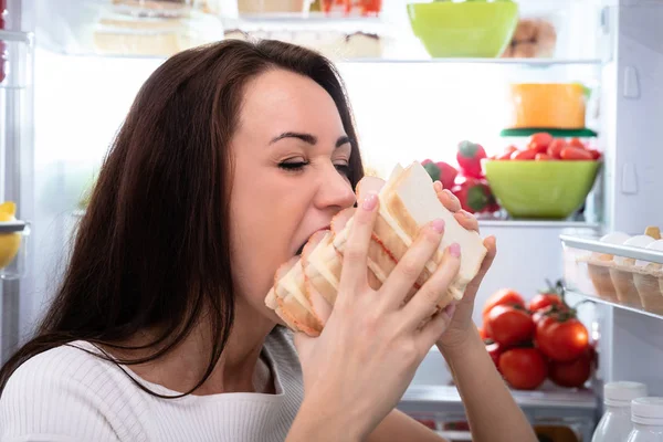 冷蔵庫の近くのサンドイッチを食べて空腹若い女性のクローズ アップ — ストック写真