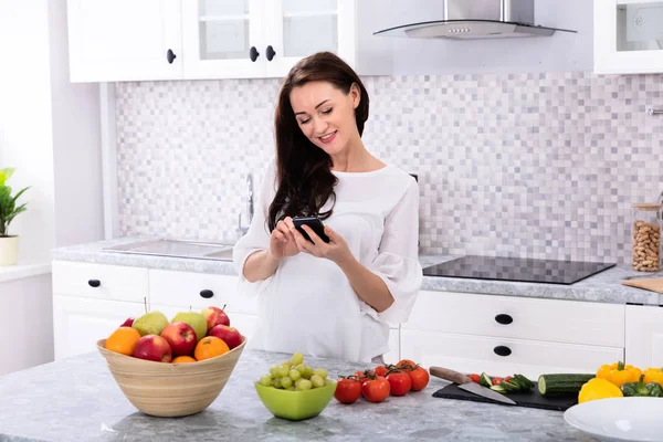 Sorrindo Jovem Mulher Usando Celular Perto Frutas Frescas Legumes Balcão — Fotografia de Stock