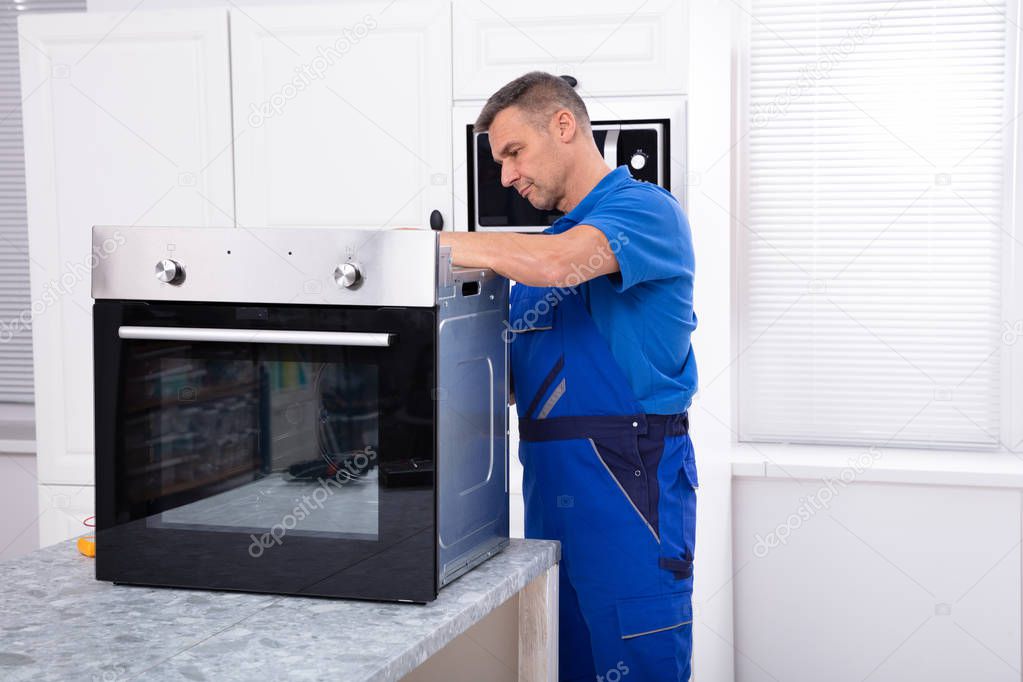 Mature Male Technician Repairing Oven On Kitchen Worktop