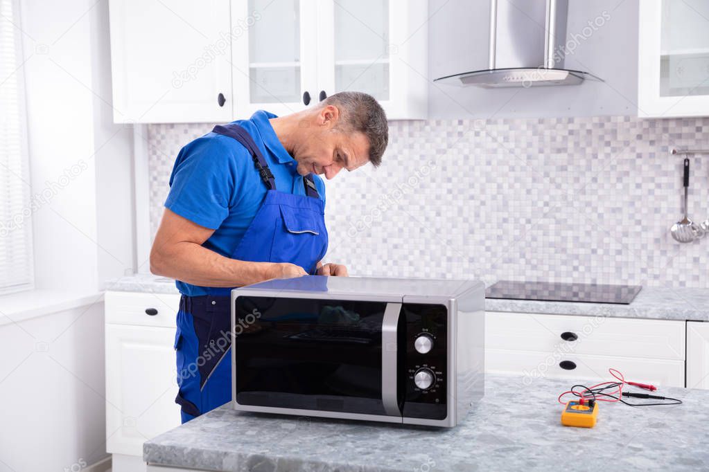 Side View Of Mature Man Repairing Microwave Oven In Kitchen