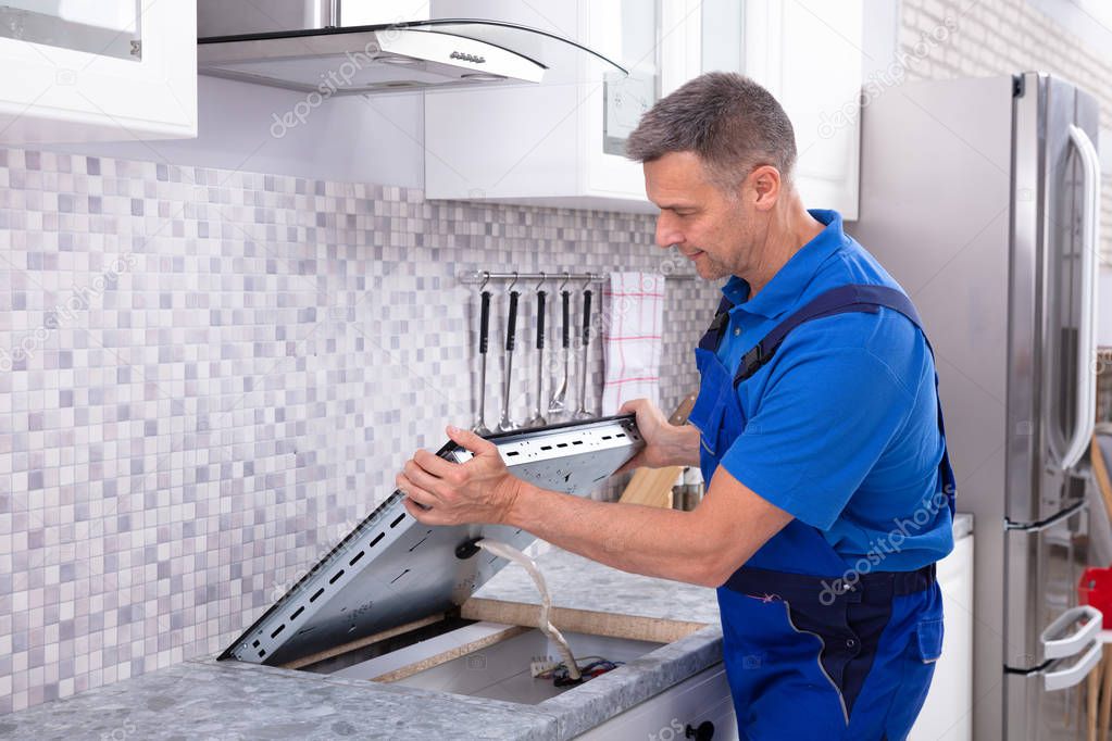 Mature Repairman Installing Induction Stove In Kitchen