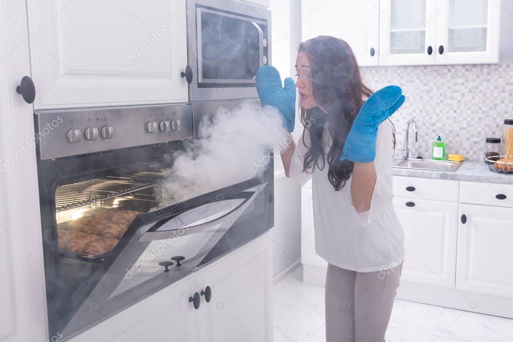 Astonished Woman Standing In Front Of Burning Oven With Smoke Around Kitchen