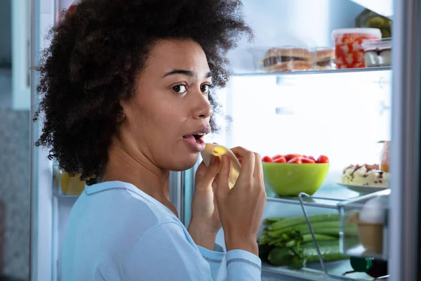 Young African Woman Eating Slice Cheese Open Refrigerator — Stock Photo, Image