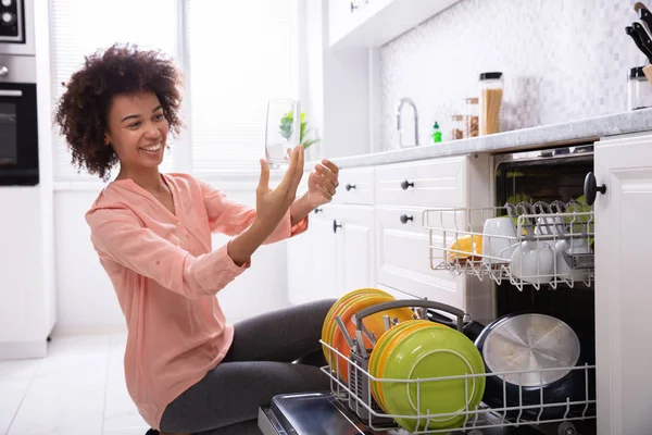 幸せな若い女チェック洗浄食器洗い機に近い透明なコップ ロイヤリティフリーのストック写真