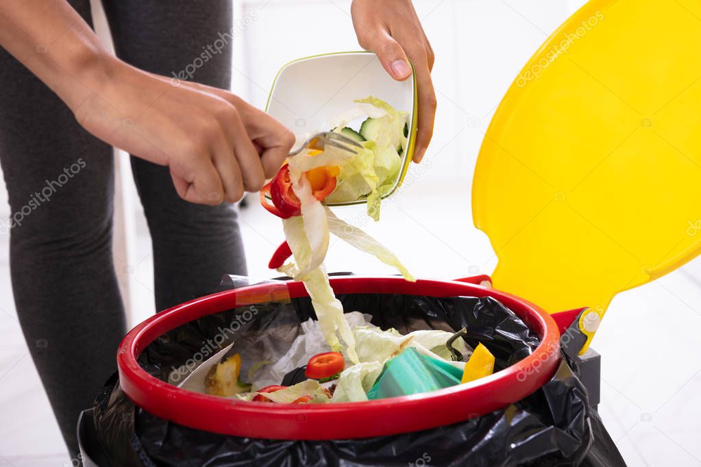 Close-up Of A Woman's Hand Throwing Salad In The Open Trash Bin