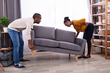 Kanepeyi kaldırırken sırtı ağrıyan Afrikalı bir adam karısına bakıyor.