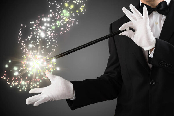 Close-up Of A Magician's Hand Creating Sparkles With Magic Wand On Grey Background