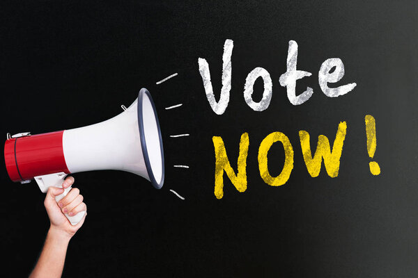 Человек, держащий мегафон рядом с желтым и белым цветом голосовать теперь текст на черном фоне
