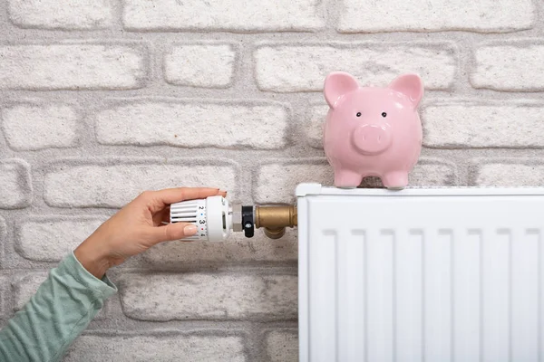 Piggy Bank radyatörü ile insan elinin termostatı ayarladığı yakın plan.