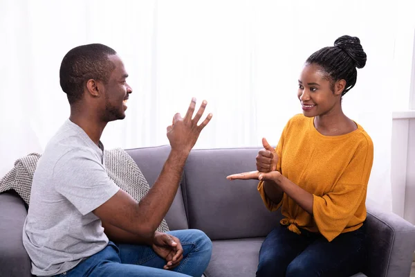 Sorrindo Jovem Casal Sentado Sofá Comunicando Com Línguas Gestuais — Fotografia de Stock