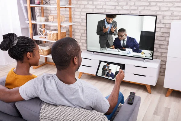 デジタルタブレット上のワイヤレスを介してソファ接続テレビチャンネルに座っているアフリカのカップル — ストック写真