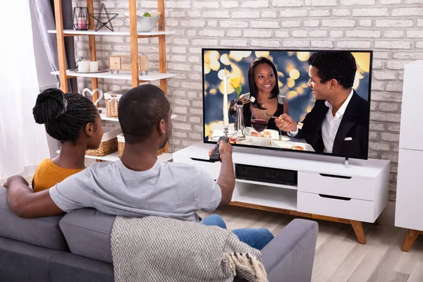 家庭でソファに座っている幸せなアフリカのカップル テレビを見て — ストック写真