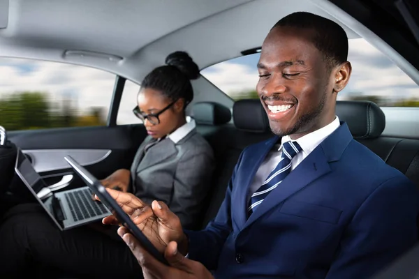 Dos Empresarios Africanos Felices Usando Dispositivos Electrónicos Mientras Viajan Coche —  Fotos de Stock