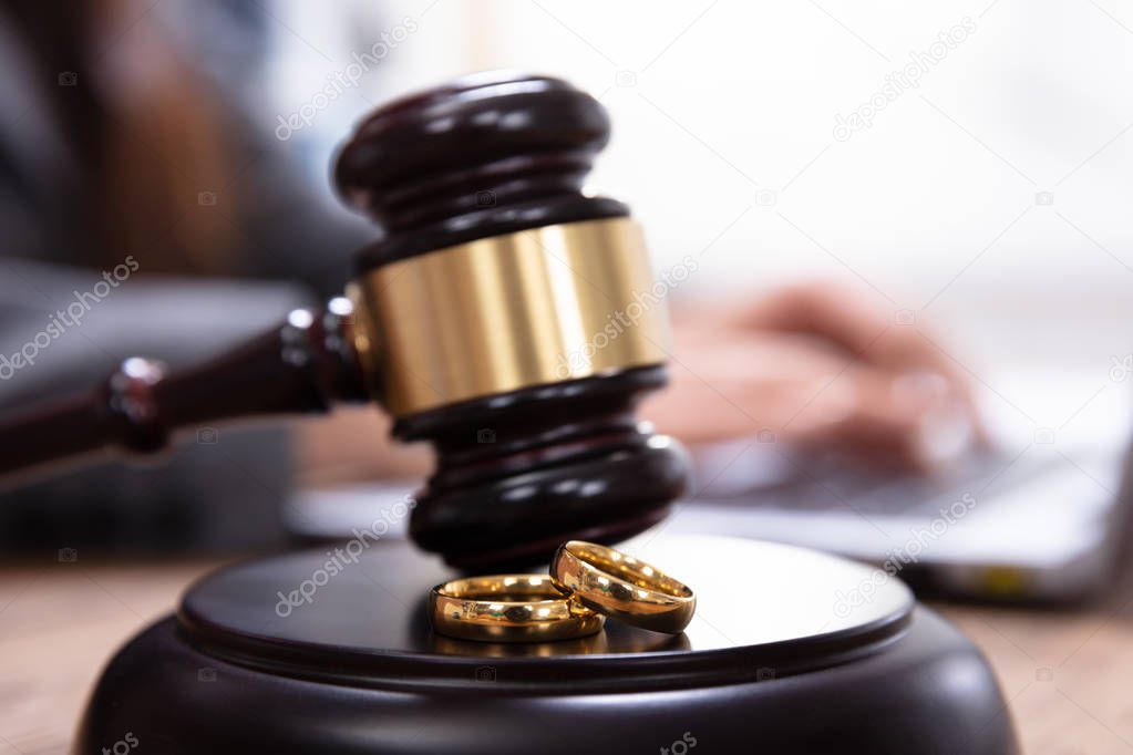 Closeup Of Golden Wedding Rings On Wooden Mallet At Table In Courtroom