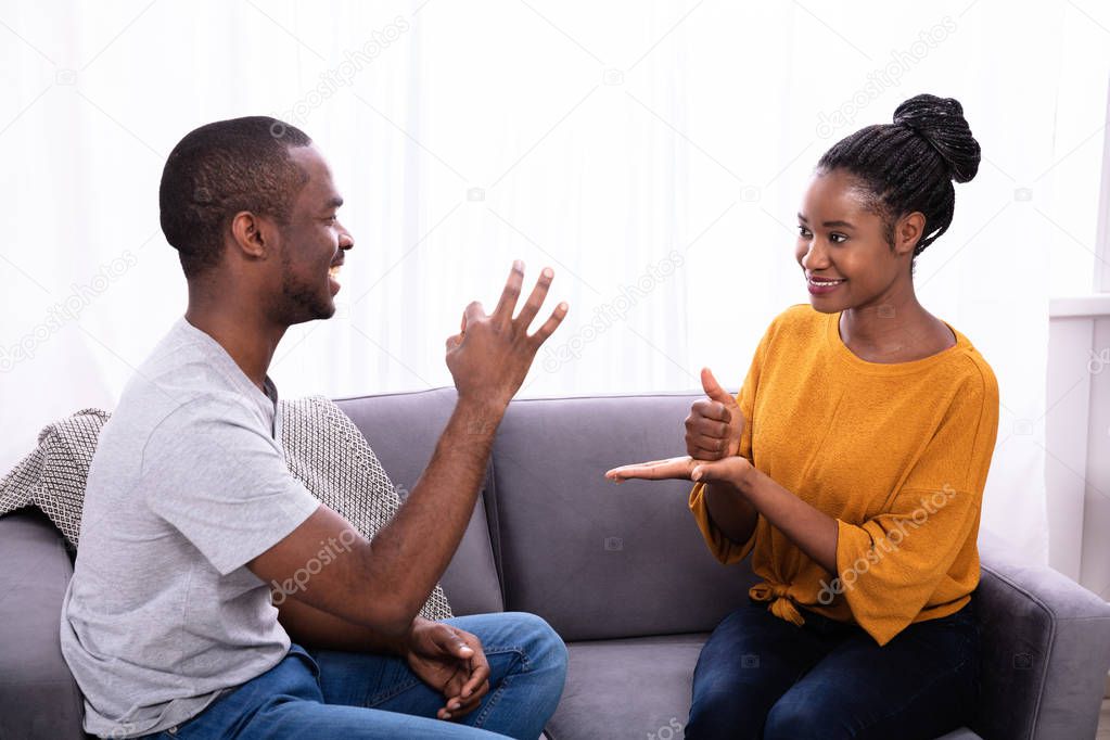 Smiling Young Couple Sitting On Sofa Communicating With Sign Languages