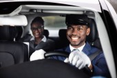 Geschäftsfrau sitzt hinter glücklichem afrikanischen Chauffeur am Steuer